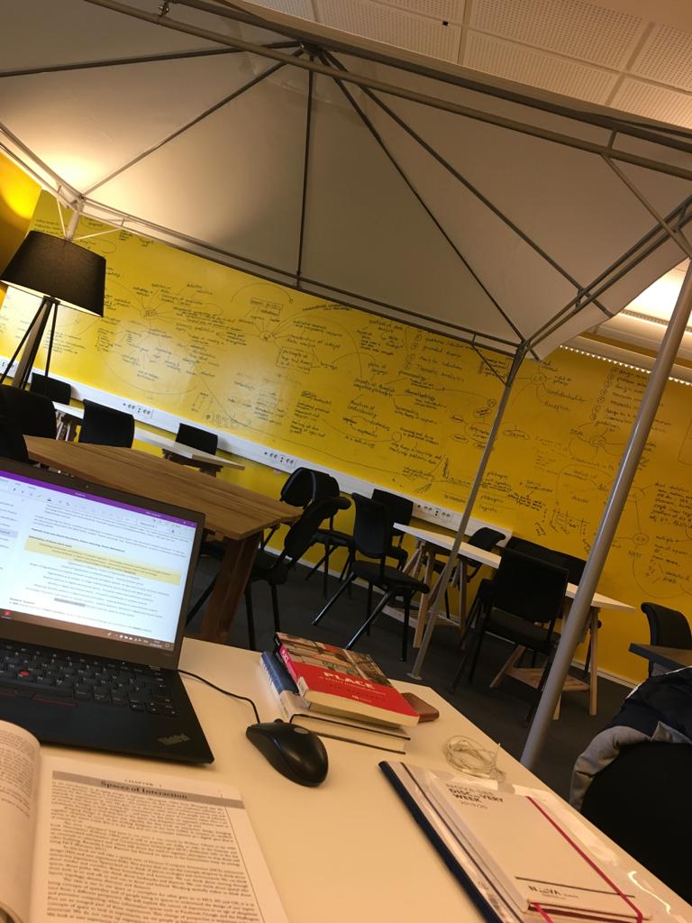 Laptop mit Masterarbeit vor einer mit Notizen vollgeschriebenen gelben Wand